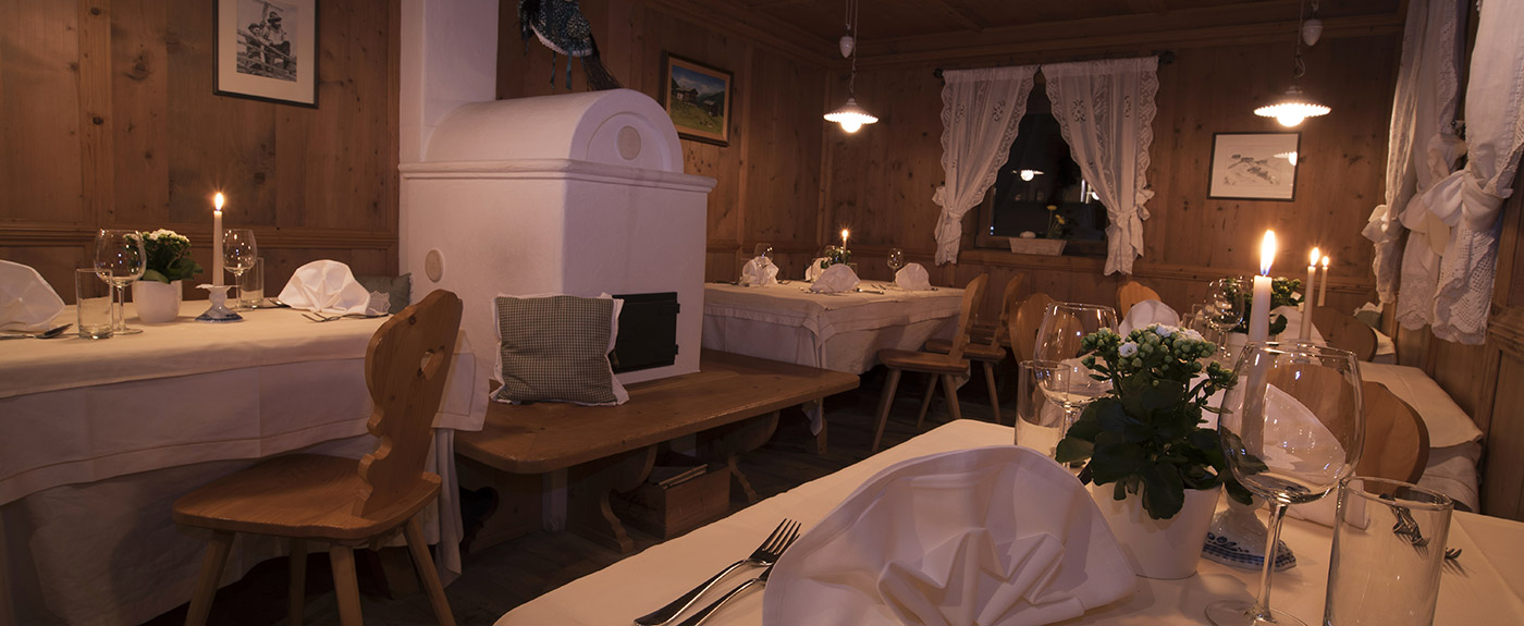 Das Innere der Stube im Hotel Arnstein mit Kachelofen und gedeckten Tischen im Kerzenlicht
